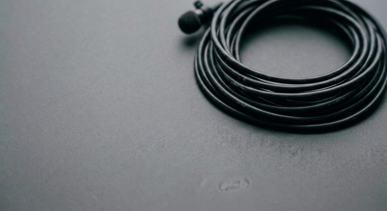 A coiled lavalier microphone cable on a gray surface